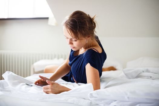 Elegant, smart, young woman using her tablet computer in bed (shallow DOF; color toned image)