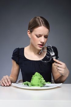 Young girl sitting over a plate of vegetables and put into the mouth barbed wire.