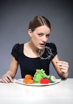 Young girl sitting over a plate of vegetables and put into the mouth barbed wire.