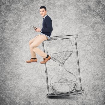 Asian young man sit on a hourglass and use tablet, concept of time management, technology, plan etc.