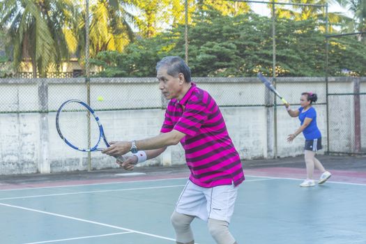 SURAT THANI, THAILAND - MARCH 1: Mixed doubles player hitting tennis ball with partner standing near net  at Chaiya tennis court on March 1, 2014 in Surat Thani, Thailand.
