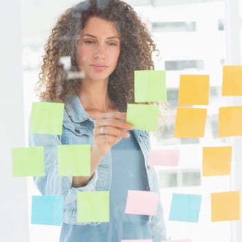 Focused designer looking at sticky notes on window in creative office