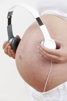 Close Up Of Pregnant Woman Holding Headphones Over Belly