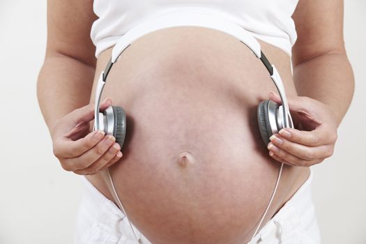 Close Up Of Pregnant Woman Holding Headphones Over Belly