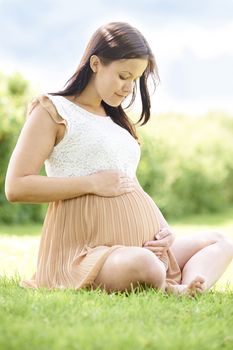 Pregnant Woman Sitting On Grass Outdoors Holding Bump