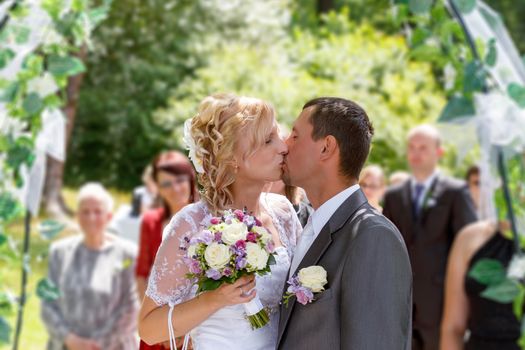 beautiful young wedding couple, blonde bride kissing her groom outdoor