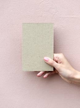 Greeting card in woman hand on wall background