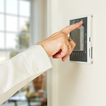 Caucasian female hand pressing button on a modern electronic thermostat timer on wall of a modern home with focus on the screen and fingers of the woman