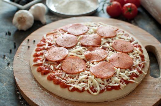Fresh dough with pepperoni on a chopping board 