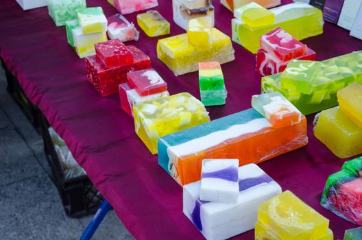 natural multicolor handmade soap tablet with medicinal herbs sold in outdoor market. Autumn city fair. Customers buying goods.