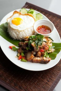 Traditional Thai dish crispy pork with a fried egg atop the jasmine rice served with chili sauce.