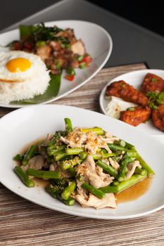 Freshly prepared Asian style chicken and asparagus stir fry with garlic and a variety of other Thai food dishes in the background.