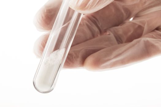 White powder in test tube held by fingers in latex gloves.