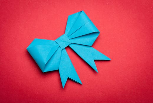 blue origami paper bow on red paper background