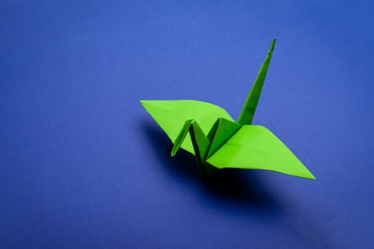 green origami paper crane on blue paper background