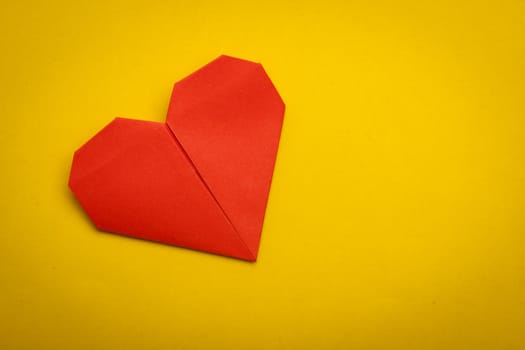 red origami paper heart on yellow paper background