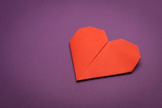 red origami paper heart on purple paper background