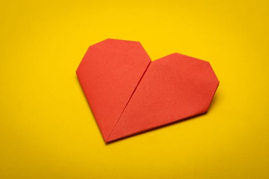 red origami paper heart on yellow paper background
