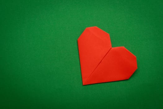 red origami paper heart on green paper background