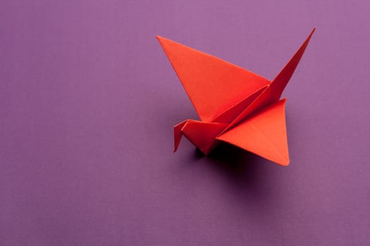 red origami paper crane on purple paper background