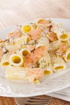 Pasta with salmon on white vintage plate on wooden background. Culinary healthy eating. 