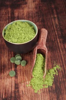 Green food supplements. Chlorella, spirulina and wheat grass on wooden scoop on wooden background. Alternative medicine. 