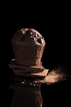 Chocolate muffin on chocolate bar with cocoa powder isolated on black background. Delicious gourmet sweet dessert eating. 