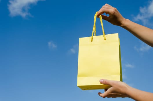 woman hand hold yellow paper gift bag on blue sky background