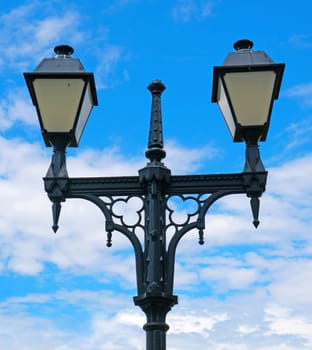   Ancient black lantern on a background of blue sky and white clouds                             