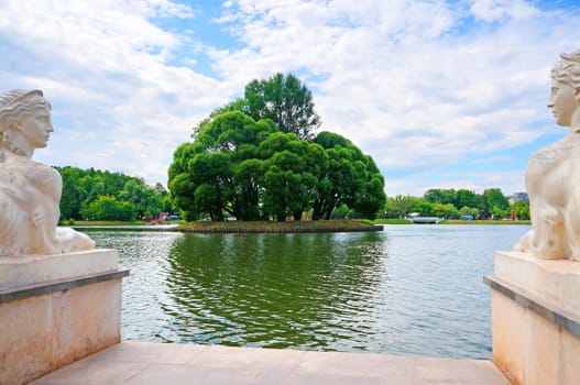 Two marble sphinx sides and island with trees on the pond                               