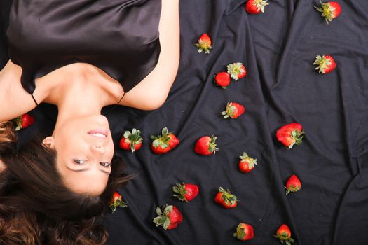 A young adult american woman smiling in a bed full of strawberries.
