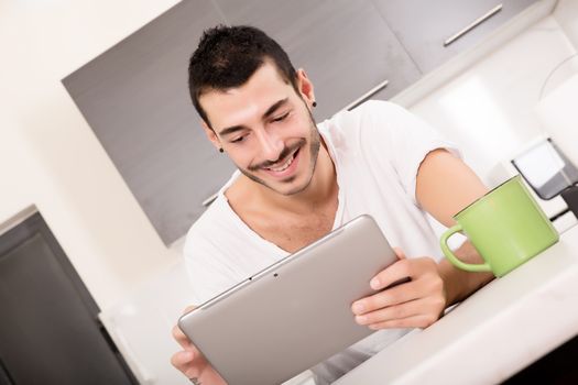 A young male sitting in the kitchen with a Tablet PC.