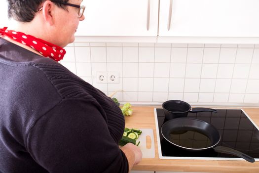 Mature overweight woman cutting cucumber in the kitchen.
