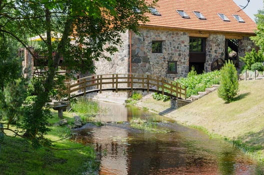 park landscape with wooden bridge over stream and ancient architectural brick manor