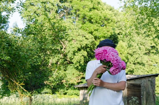 man hiding his face with large pink peony bouquet of spring garden