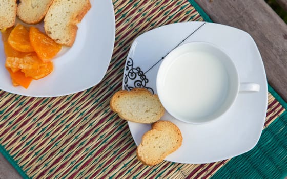Warm milk in the white cup and tangerine marmale with dried bread