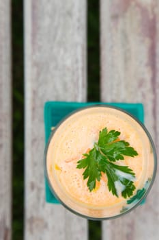 A glass of carrot smootie with fresh parsley leaves on the wooden surface.top view