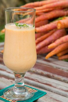 A glass of carrot smoothie with fresh parsley. Fresh carrots in the background