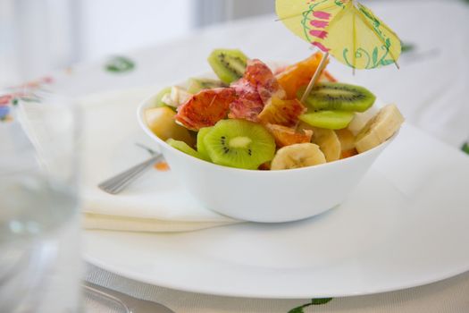 A white plate of fruit salad with small decorative umbrella on the festive table