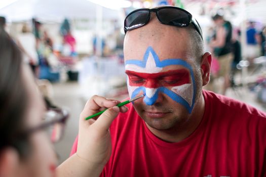 McDonough, GA, USA - May 10, 2014:  A man gets a Lafleur symbol painted on his face at the annual Dog Days of McDonough festival.