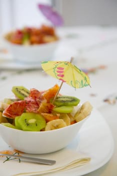 A white plate of fruit salad with small decorative umbrella on the festive table