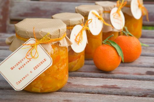 Handmade tangerine marmalade in the glass and two fresh tangerines on the old wooden surface