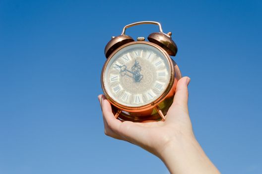 antique bronze clock with roman numerals in woman hand on blue sky background