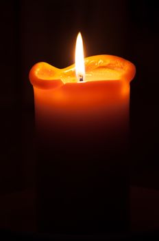Lit orange candle over dark black background