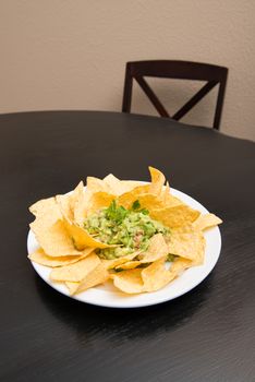 Green mexican salsa guacamole and yellow corn tortilla chips on the dining table