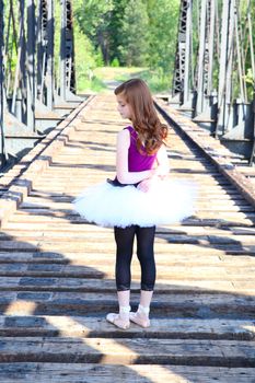 Beautiful girl wearing a white tutu standing on a bridge 