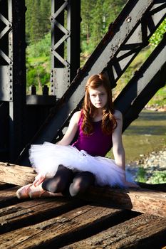 Beautiful girl wearing a white tutu sitting on a bridge 