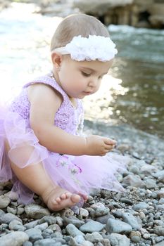 Beautiful brunette baby girl sitting on pebble beach