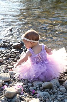 Beautiful brunette baby girl sitting on pebble beach