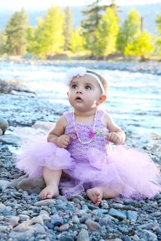 Beautiful brunette baby girl sitting on pebble beach